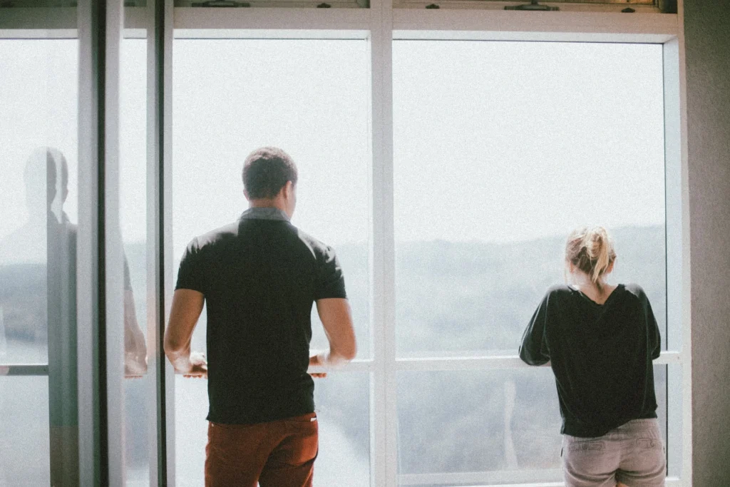 A couple gazes out of a window, sharing a moment of reflection and connection in a cozy indoor setting, symbolizing tenant retention and the value of creating a comfortable, lasting home.