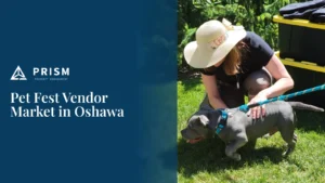 A woman in a sun hat interacts with a gray dog on a leash in a grassy area, with text 'Pet Fest Vendor Market in Oshawa' and a 'Prism Property Management' logo on a blue background